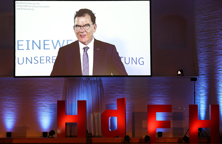 Bundesentwicklungsminister Dr. Gerd Müller ist auf einer Leinwand zu sehen; darunter in rot angestrahlt die Buchstaben HdFH.